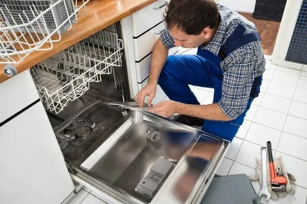 Technician inspecting a dishwasher door with repair tools nearby