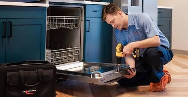 Technician repairing an open dishwasher beside blue kitchen cabinets